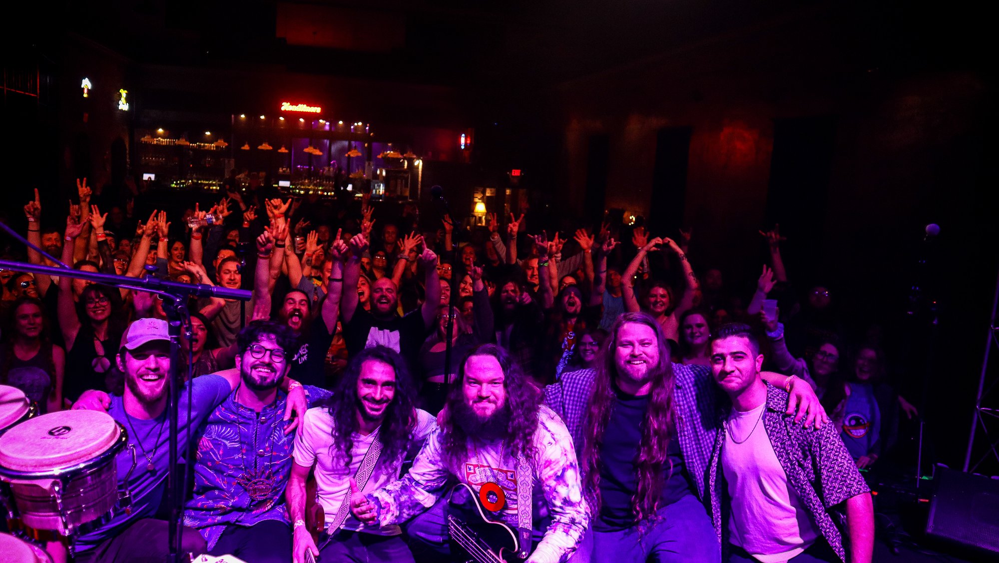 Band and crowd group photo after show with hands raised and purple stage wash