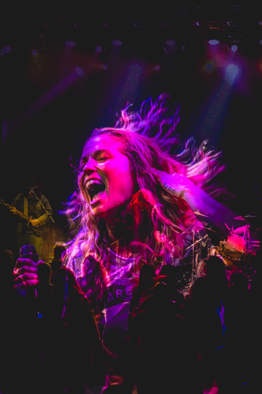 Vocalist Hayley Jane mid-scream with hair flying under magenta and purple stage wash
