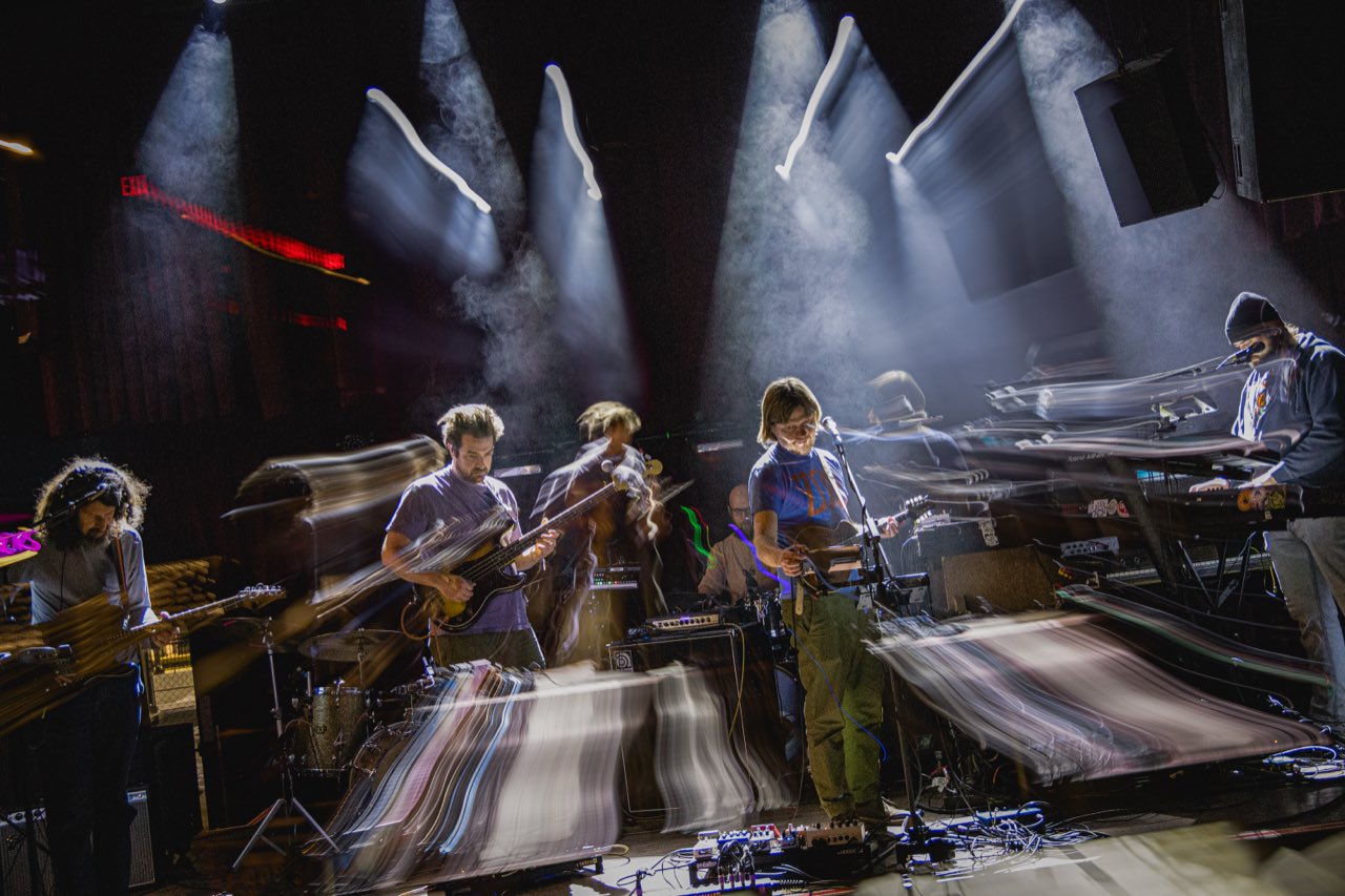 Houseplant full band with long-exposure motion blur, smoke, and white spotlights cutting through the stage