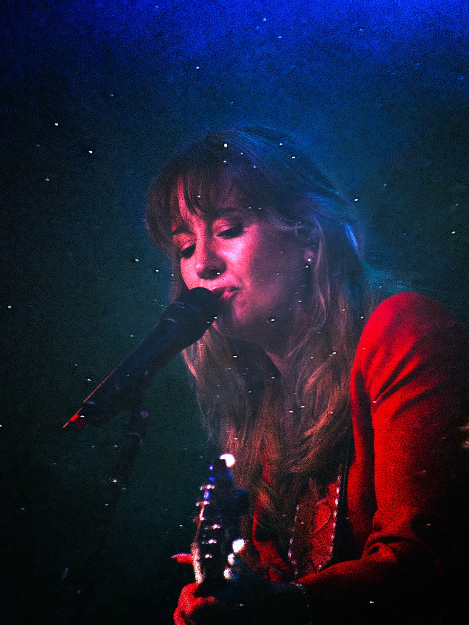 Margo Price singing into microphone in soft blue and red stage light with floating dust particles